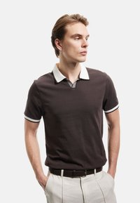 Donkerbruine polo met een witte kraag en manchetten, met een V-halsontwerp en textuuraccenten. Gedragen met lichte broek.