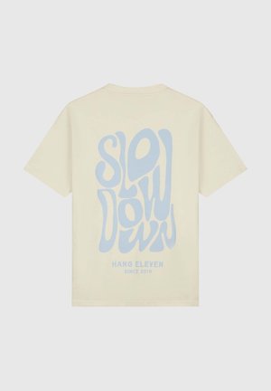 Cream-colored cotton t-shirt featuring large, stylized blue typography of "SLOW DOWN" and "HANG ELEVEN SINCE 2019" on the back.