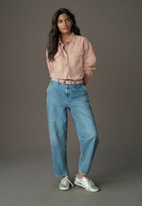 Camicia di denim rosa chiaro con due tasche sul petto, abbinata a jeans blu a vita alta e sneakers argento con suole e lacci bianchi.