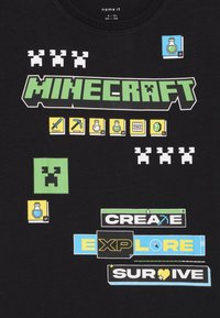 Black cotton t-shirt featuring colorful "Minecraft" graphic with tools, potions, and text saying "CREATE EXPLORE SURVIVE." Classic crew neck design.