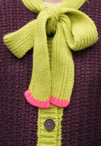 Megzta tamsiai violetinė kardiganas su žaliu raišteliu prie iškirptės, papuoštas rožiniais akcentais ir viena ruda saga priekyje.