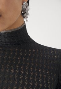 Haut en dentelle noire avec un col montant orné d'un accent métallique. Boucles d'oreilles en cristal scintillantes avec des chaînes cascades et un motif complexe.