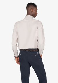 Camisa de manga larga color beige claro con cuello alto; combinada con pantalones azul marino y un cinturón trenzado. La tela parece suave y ligera.