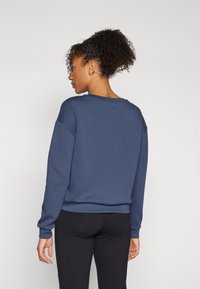 Felpa blu navy con una vestibilità rilassata, collo a giro e maniche lunghe. Presenta una texture liscia e polsini a coste. Leggings neri indossati sotto.