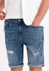 Denimshorts i blekt blått med en klassisk passform, med slitna accenter, uppvikta fållar och synliga söm detaljer.