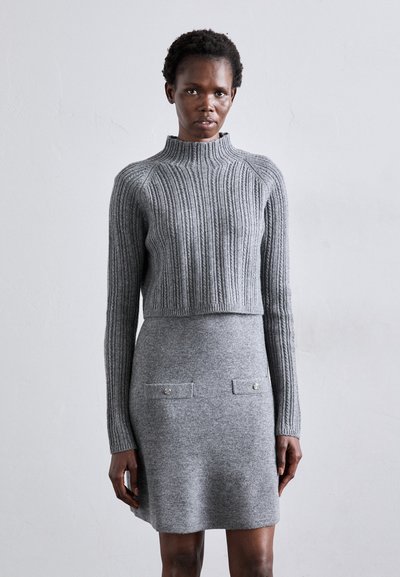 Gray ribbed knit sweater with high neckline paired with a smooth gray dress featuring two front pockets and decorative buttons.