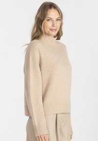 Beżowy sweter z golfem wykonany z miękkiego, teksturowanego materiału. Posiada ściągacze przy rękawach i na dole, a także luźny, prostokątny fason.