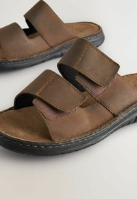 Sandales en cuir marron avec deux sangles Velcro réglables, semelle intérieure douce, surface texturée et semelle en caoutchouc noir.