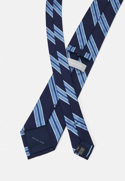 Cravate marine avec des rayures diagonales bleues, fabriquée en tissu texturé. Comprend une étiquette de marque. Les extrémités sont pointues avec un détail de couture supplémentaire.