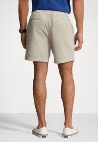 Beige kordflourshorts med elastisk midja, med två bakfickor och en fåll som slutar ovan knäet. Bärs med vita slip-in skor.