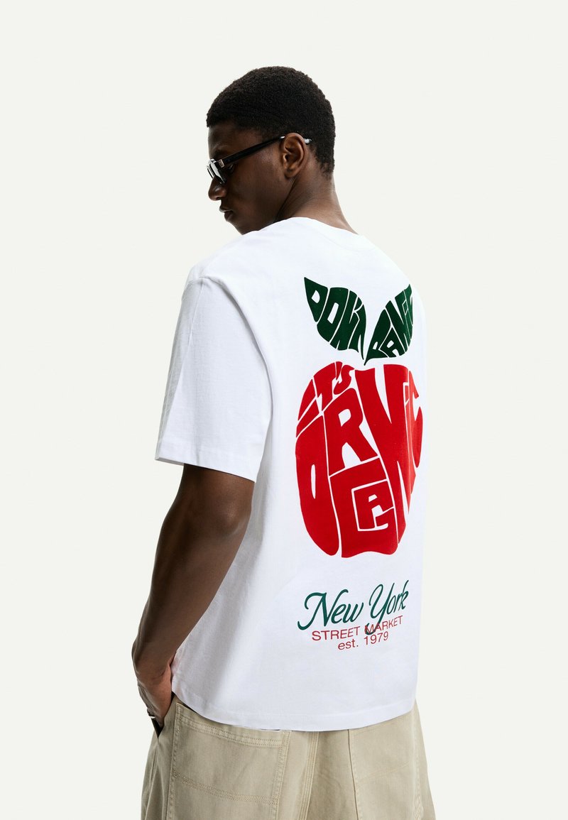 T-shirt in cotone bianco con una grande grafica di una mela rossa con una foglia verde e il testo "New York Street Market est. 1979" sul retro.