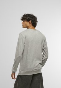 Sweatshirt gri cu mânecă lungă, fabricat dintr-un amestec moale de bumbac, cu un guler și manșete ribbate, având o croială lejeră și fără logo-uri vizibile.