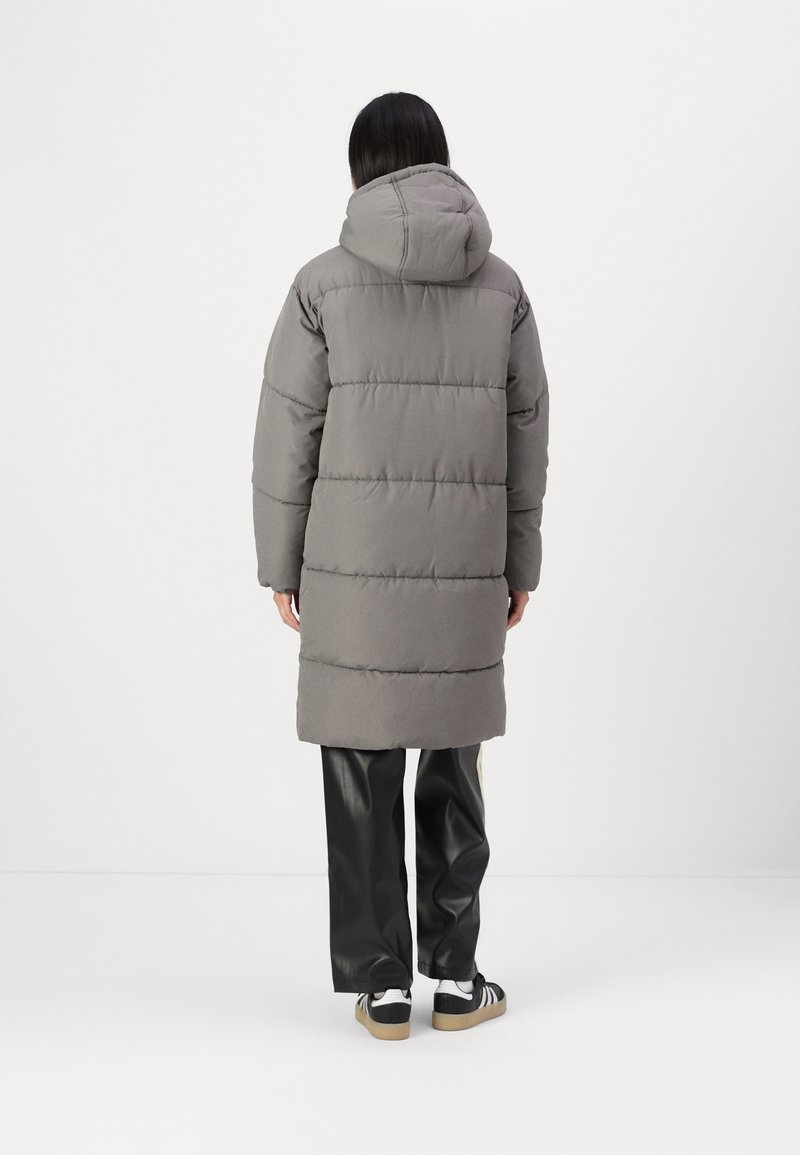 Grau gefütterter Mantel mit Kapuze, mit horizontalen Steppnähten, langer Länge und lockerer Passform. Trägt man über schwarzen Kunstlederhosen.