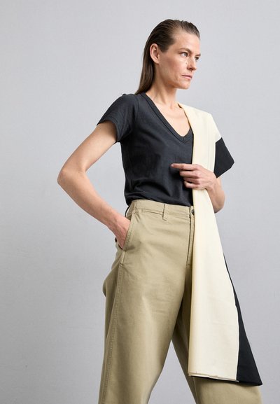 Black V-neck T-shirt, cotton material, paired with light khaki wide-leg pants, featuring a long cream and black draped detail.