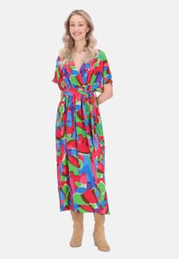 Rochie înfășurată colorată, cu model, prezent�ând forme abstracte în nuanțe de roșu, verde și albastru, cu decolteu adânc în V și talie evidențiată cu o curea, asortată cu cizme bej.
