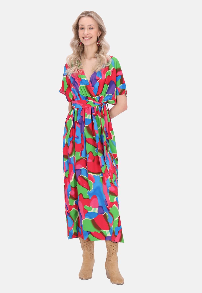 Rochie înfășurată colorată, cu model, prezentând forme abstracte în nuanțe de roșu, verde și albastru, cu decolteu adânc în V și talie evidențiată cu o curea, asortată cu cizme bej.