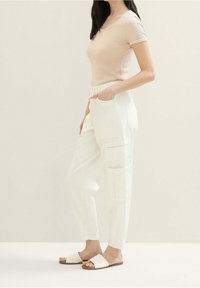 Beige fitted top met korte mouwen, gecombineerd met witte cargobroek met zijzakken. Complementeert met platte beige instapsandalen.