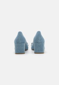 Chaussures en denim à talons bloc, avec une pointe effilée, présentant une texture bleu clair et des détails de couture subtils sur les côtés.