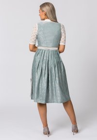 Ein hellblaues Kleid aus einem strukturierten Stoffmuster, mit Falten im Rücken und einer kontrastierenden weißen Bluse mit Spitzenärmeln.