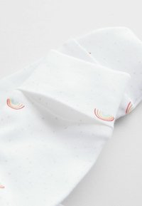 Chaussettes blanches avec une petite texture en points et des motifs d'arc-en-ciel en rouge, bleu et jaune sur les côtés. Tissu doux, forme classique.