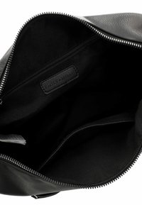 Intérieur d'un sac en cuir noir avec une texture lisse, comportant un compartiment zippé et un revêtement en tissu. Une étiquette en cuir de marque est visible.