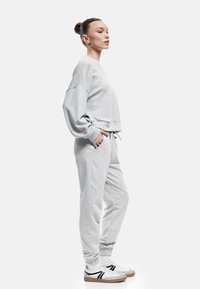 Grå cropped sweatshirt og matchende joggingbukser, blødt stof, afslappet pasform, elastiske manchetter, sidelommer, parret med hvide sneakers med sorte detaljer.