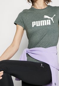 Grå bomullströja med vit "PUMA"-logotyp, i kombination med svarta leggings med en liten logotyp. Lavendelfärgad tröja knuten runt midjan.
