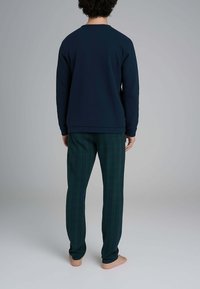 Felpa blu navy con scollo rotondo abbinata a pantaloni a quadri verdi. Il tessuto sembra morbido e i pantaloni presentano un motivo a scacchiera.