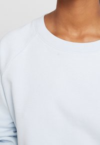 Světle modrý svetr s kulatým výstřihem, žebrovanými manžetami a měkkou, hladkou texturou. Má volný střih a raglánové rukávy.