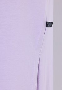 Primer plano de tela de color púrpura claro con una pequeña etiqueta negra de ropa y un detalle de abertura lateral en la costura.