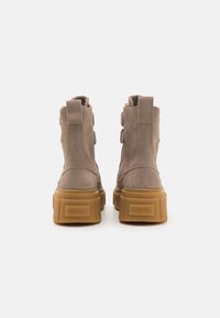 Botines de ante beige con suela de goma amarilla gruesa, que cuentan con tres correas laterales y pestañas traseras para ponérselos con facilidad.