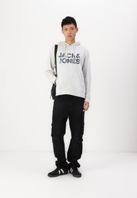 Grauer Kapuzenpullover mit "JACK & JONES"-Logo, schwarze Cargo-Hosen mit Taschen und schwarze Sneaker mit weißen Streifen. Einfaches, lässiges Outfit.