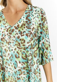 Top leggero e setoso con scollatura a V e maniche a campana. Presenta una stampa leopardata colorata in verdi, blu e marroni.