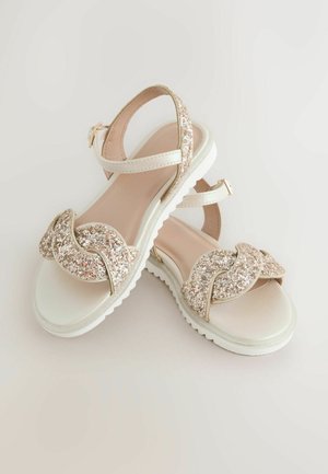 Světlé sandály s texturovaným, třpytivým páskem se zkrouceným designem, polstrovanou podrážkou a nastavitelným páskem kolem kotníku.