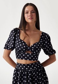 Top corto negro con lunares blancos, con mangas abullonadas, un detalle de lazo en el centro y una falda a juego con lunares.