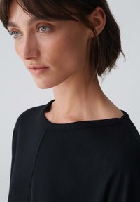 Schwarzer Pullover mit lockerem Schnitt und Bootskragen, aus weichem Material gefertigt. Mit minimalen Nähten und einer glatten Textur.