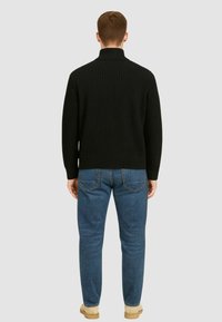 Maglione a collo alto nero a coste indossato con jeans blu. Il maglione presenta una finitura texturizzata e una silhouette aderente, con un colletto alto.