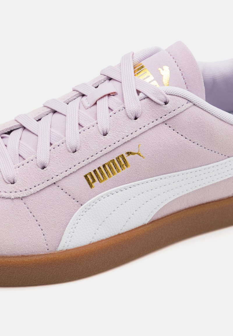 Zapatilla de ante púrpura claro con acentos blancos, que presenta el logo dorado de Puma, cordones planos y una suela de goma texturizada.