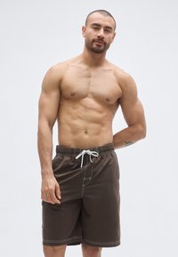 Hnedé plavecké šortky, ľahká tkanina, elastický pás s bielym sťahovacím šnúrkou, bočná kapsa, kontrastné biele stehy.