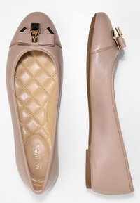 Ballerines en cuir nude avec un accent de nœud noir brillant, semelle intérieure beige matelassée et semelle en caoutchouc flexible. Texture lisse et design à orteil arrondi.