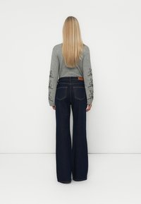Jeans de perna larga em azul escuro com uma cintura alta, combinados com um suéter cinza com bordados florais pretos nas mangas.
