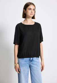 Top nero a maniche corte con scollatura rotonda e orlo arricciato, realizzato in tessuto morbido, abbinato a pantaloni in denim azzurro chiaro.