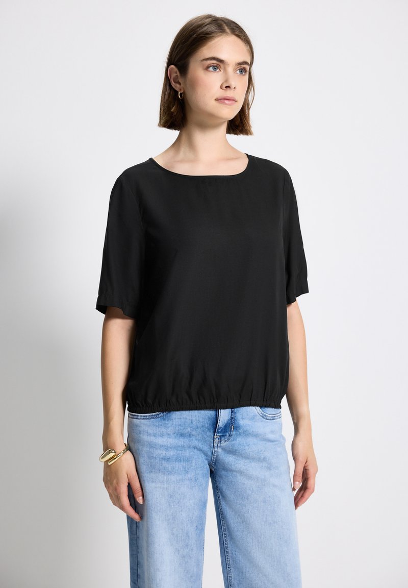 Top nero a maniche corte con scollatura rotonda e orlo arricciato, realizzato in tessuto morbido, abbinato a pantaloni in denim azzurro chiaro.