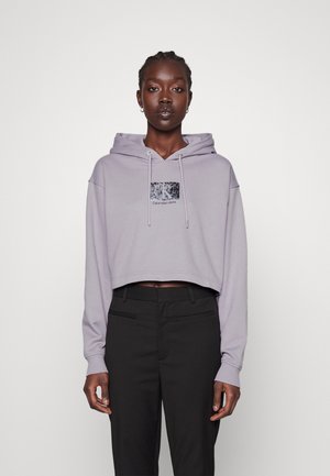 Felpa corta di un delicato colore viola con cappuccio regolabile e una patella con logo nero lucido. Abbinata a pantaloni neri sartoriali. Tessuto dalla texture liscia.
