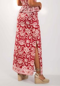 Jupe maxi rouge avec un imprimé floral blanc, détail de fente sur le côté et bord décoratif. Assortie à des wedges espadrilles de couleur claire.
