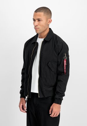 Schwarze Bomberjacke mit einem Reißverschluss vorne, einer Fronttasche und einem roten Akzent am linken Ärmel. Hergestellt aus strukturiertem Stoff mit entspannter Passform.