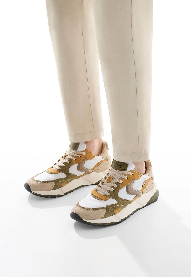 Baskets beige et olive avec un mélange de daim et de maille. Présente des panneaux blancs, des semelles épaisses et des lacets beiges. La semelle extérieure est noire.