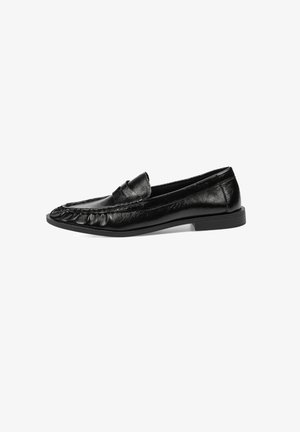 Mocasines de cuero negro con un acabado texturizado, que presentan un diseño cosido a lo largo de la punta y una suela plana de goma.
