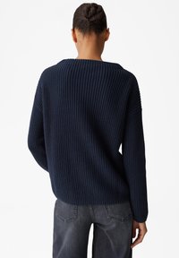 Maglione oversize lavorato a maglia di colore navy con texture a coste, scollatura ampia e spalle cadenti, abbinato a jeans grigi a vestibilità comoda.