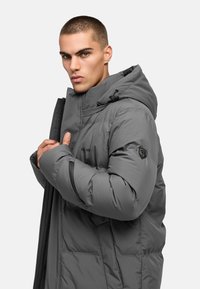 Sivá puffr jacket s kapucňou, s predným zipsom, prešitými panelmi a logom na rukáve. Mäkko izolovaný materiál.